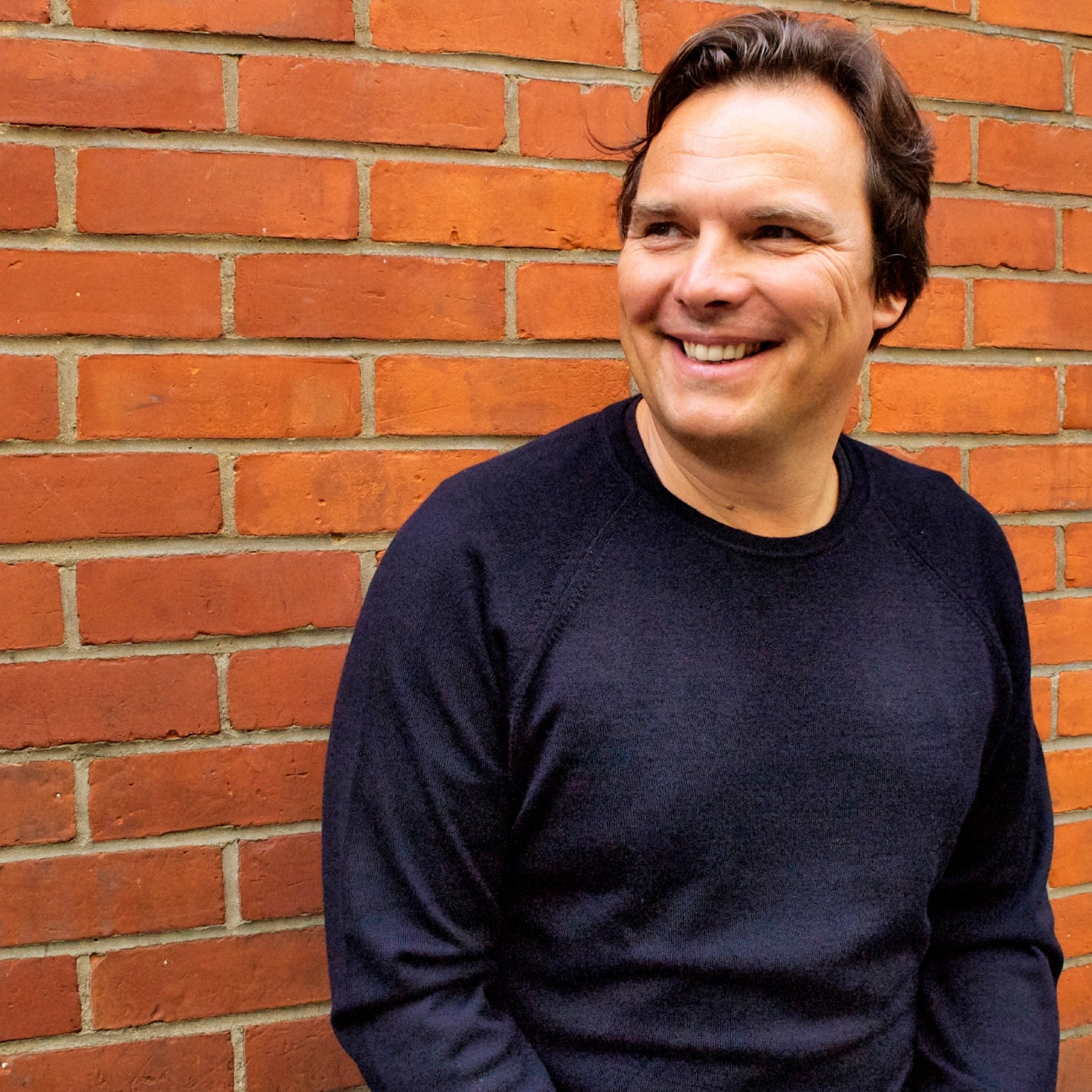 Petter Neby, founder of Punkt., smiling while leaning against a red brick wall, wearing a dark sweater.