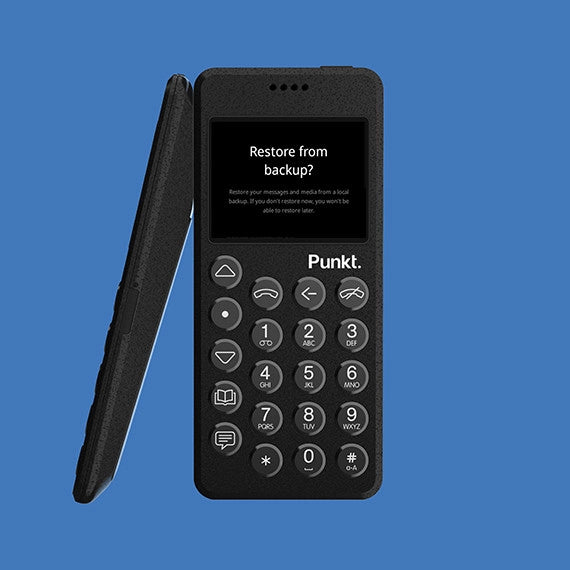 Front and side view of black Punkt. MP02 phone on blue background – Screen prompts “Restore from backup?” with a description about restoring messages and media.