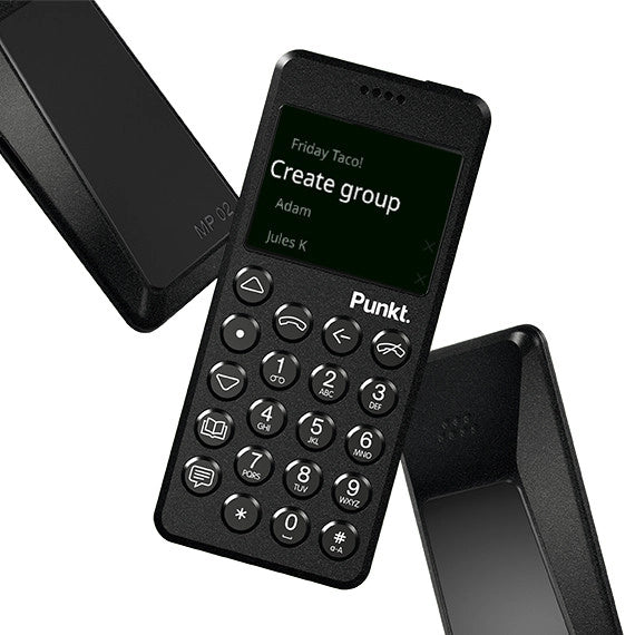 Black Punkt. MP02 phone tilted with cover pieces – Black minimalist mobile phone with round keypad and small screen displaying a “Create group” message, shown with its protective covers.