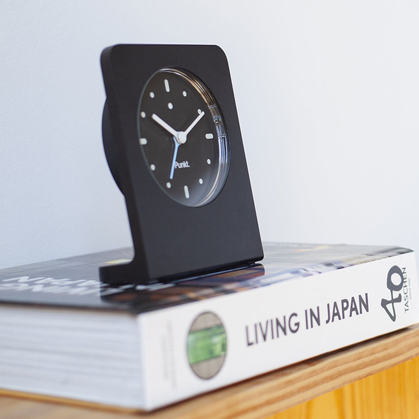 Punkt AC02 minimalist alarm clock in black, placed on top of the book "Living in Japan", reflecting elegant and timeless Japanese-inspired design.