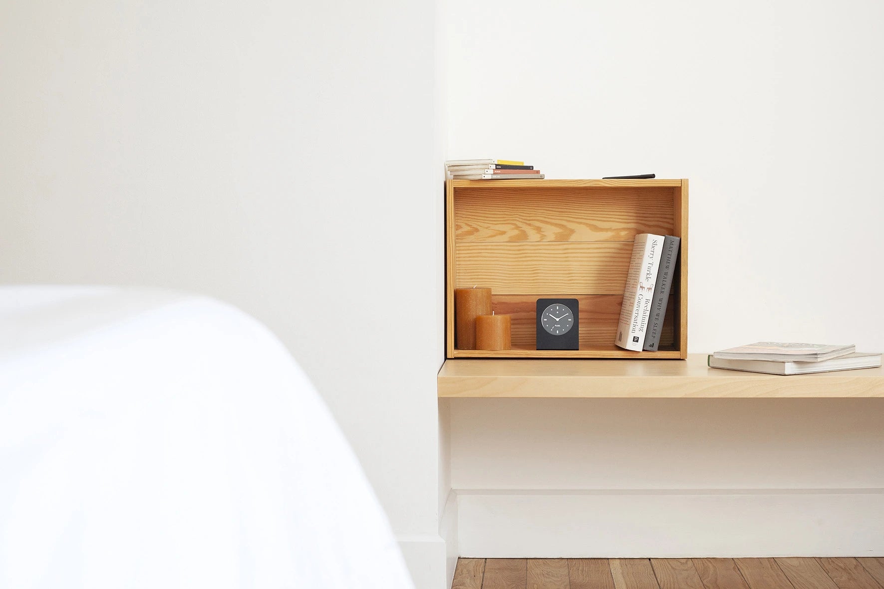 Punkt AC02 alarm clock styled on a natural wooden shelf alongside books and candles, creating a calm and warm bedroom setting.