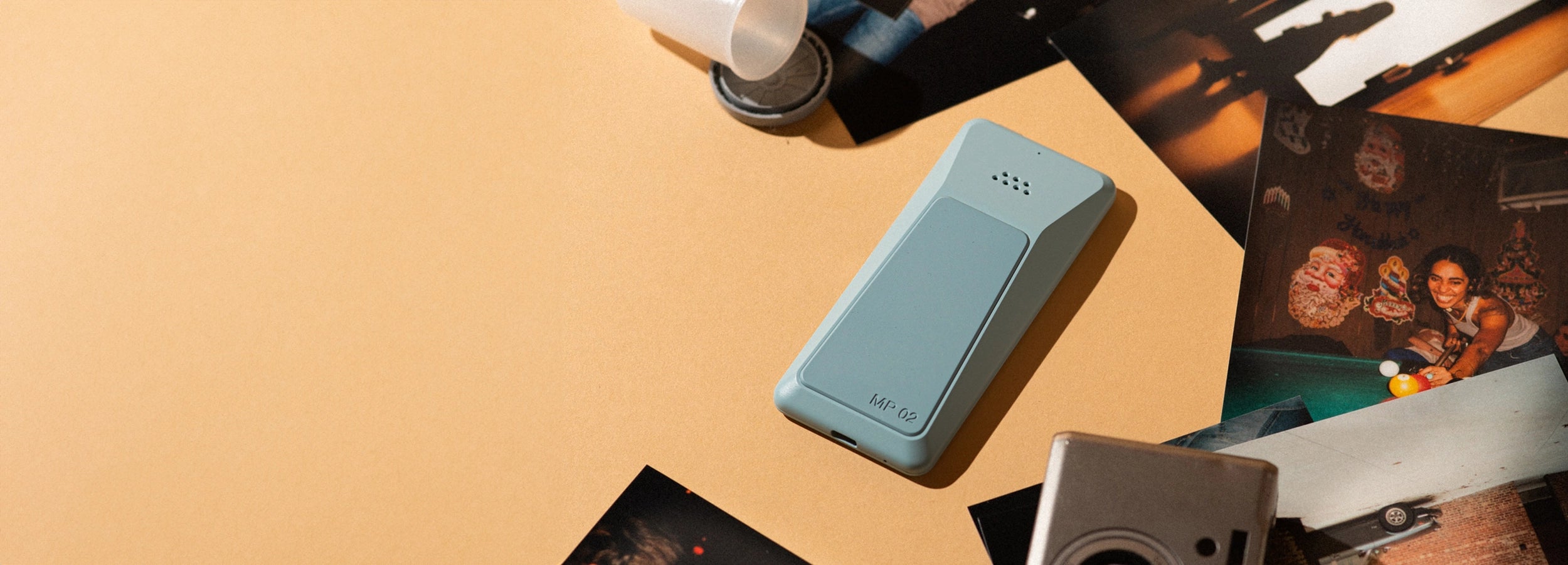 Punkt. MP02 minimalist phone in blue, placed on a beige surface among analog photographs and a vintage camera.