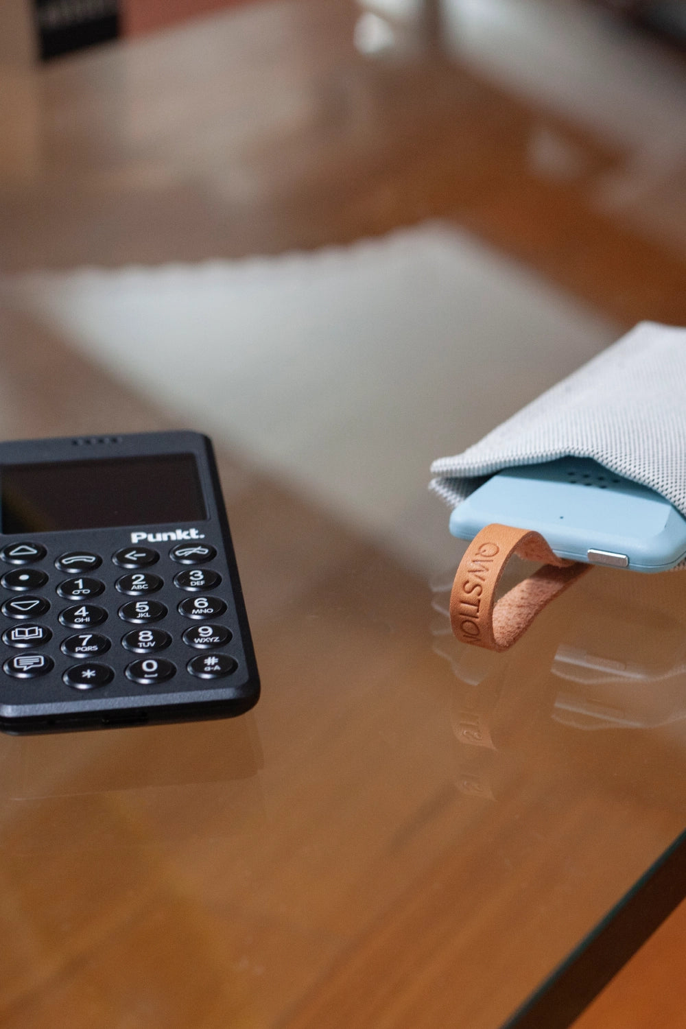 Black Punkt. MP02 next to its fabric QWSTION case with the phone partly inside, leather tag branded with QWSTION visible.