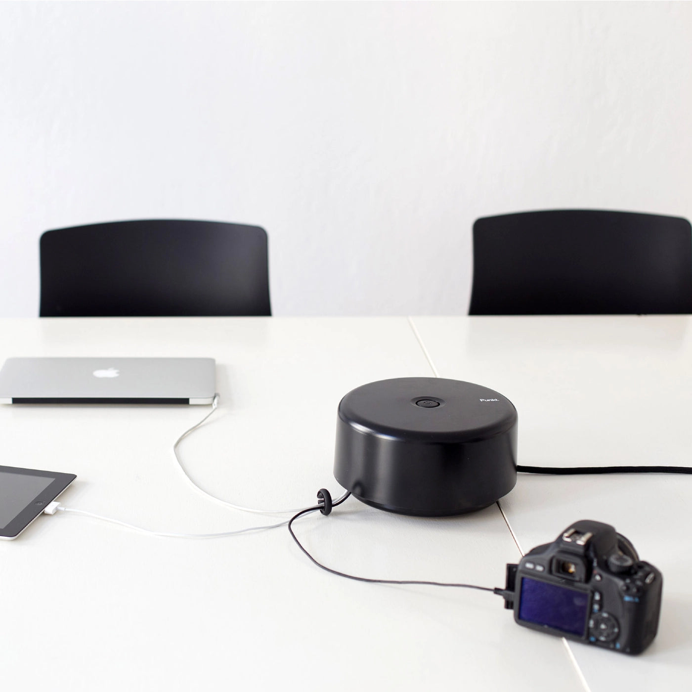 Punkt. ES01 power strip in black on a white table, connected to a camera and other devices in a minimal workspace.