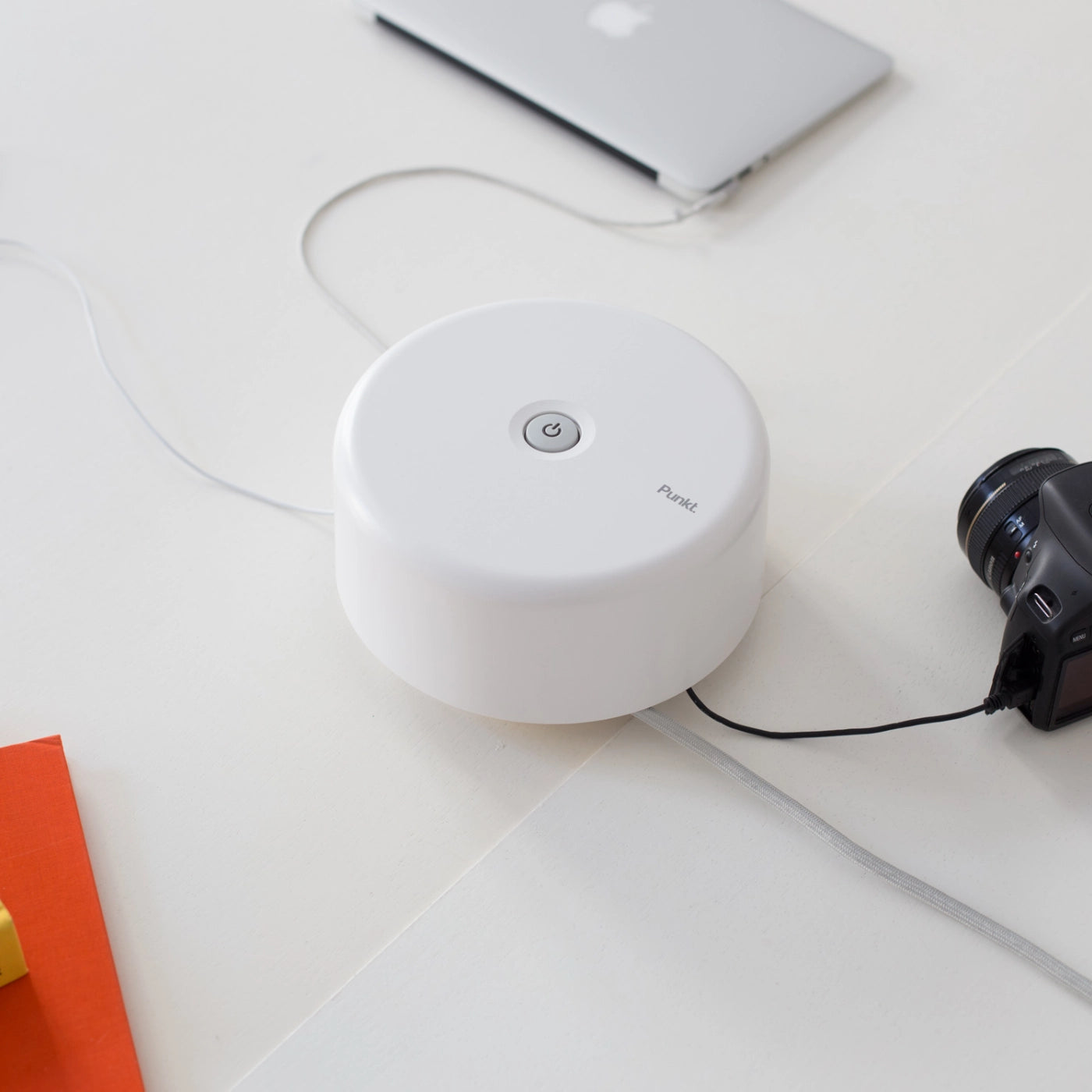 Side view of the white Punkt. ES01 in a minimal desk setup, powering a MacBook and tablet, with a DSLR camera connected.