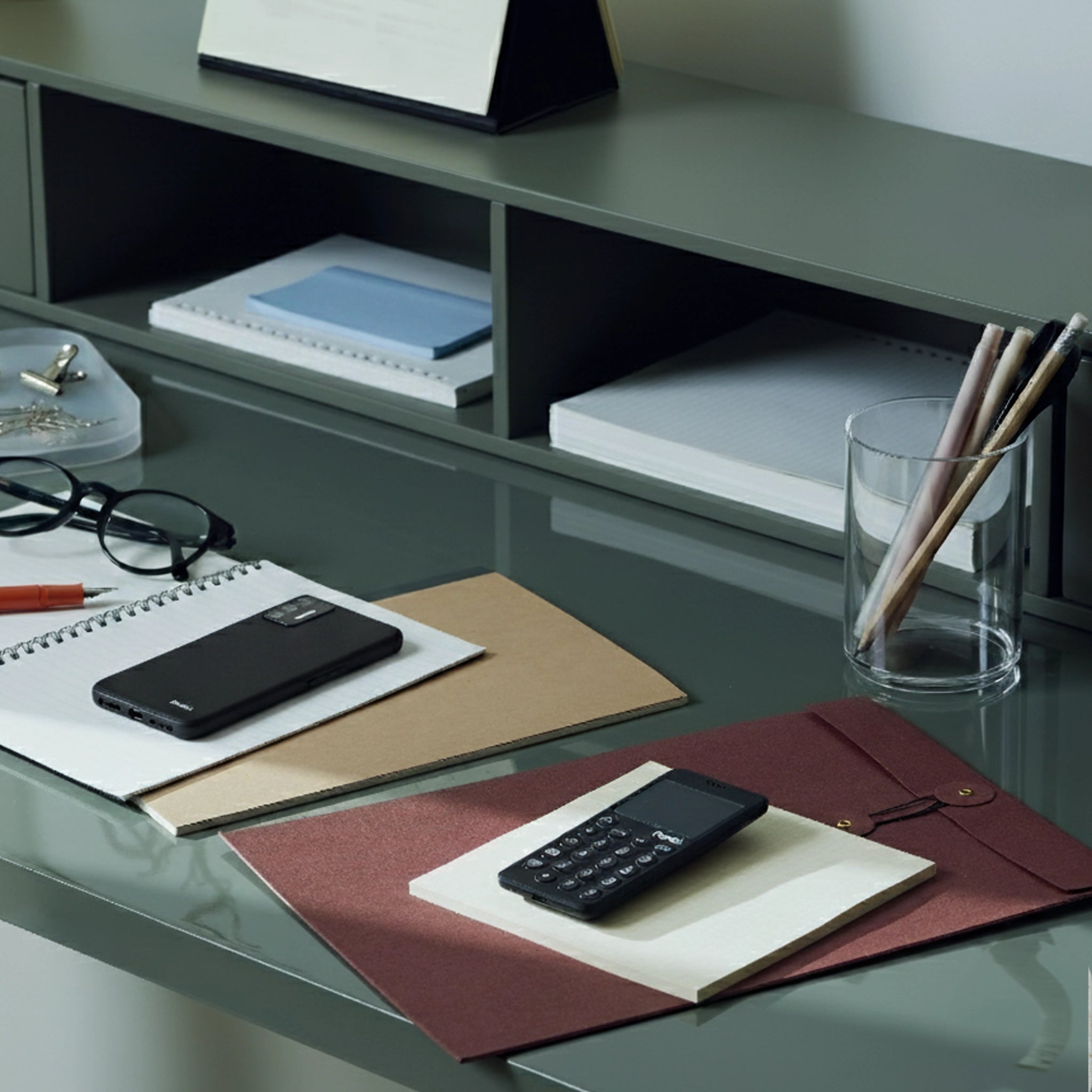 A tidy desk with two minimalist black phones, notebooks, and stationery items, including pencils and glasses.