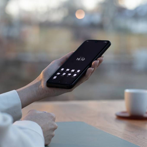 Person holding a smartphone at a table, screen showing dark minimalist app layout.