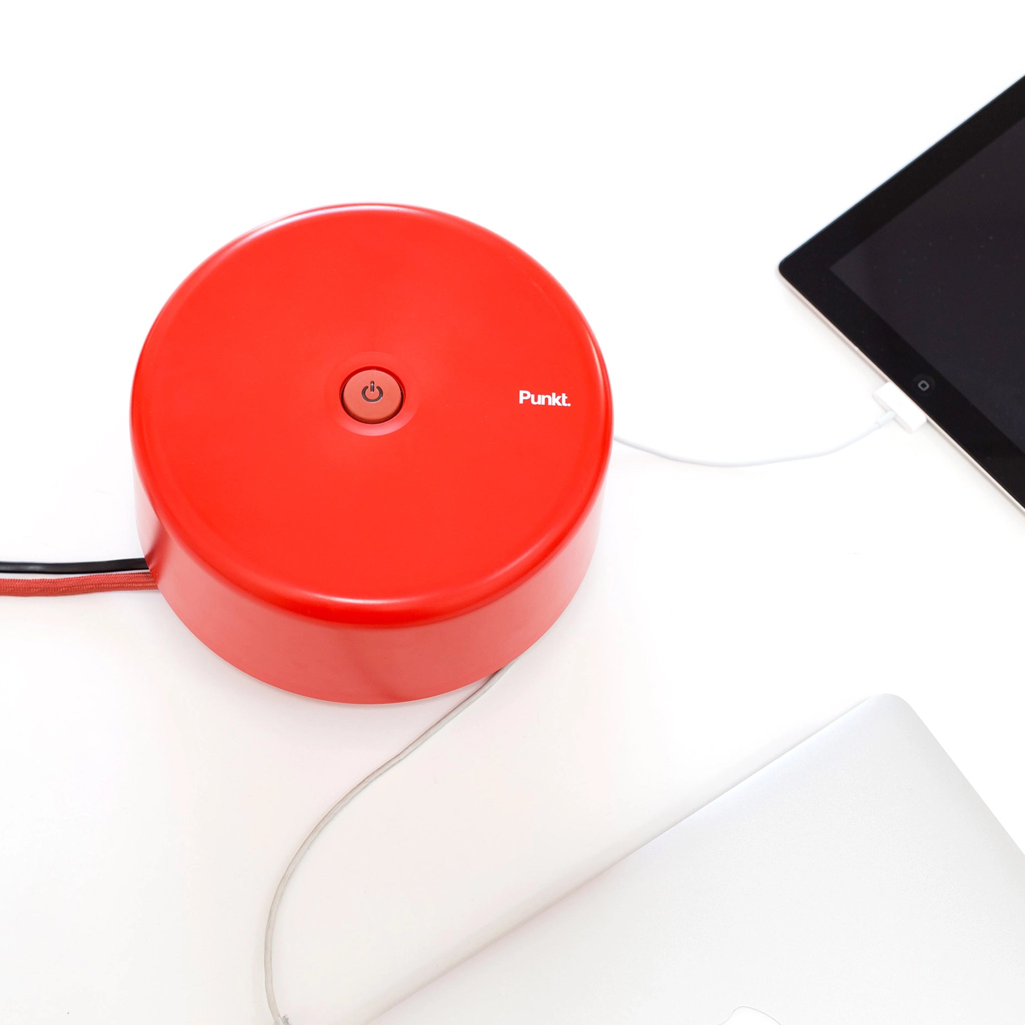 Red Punkt. ES01 extension socket with a power button, powering a tablet and laptop on a white surface.