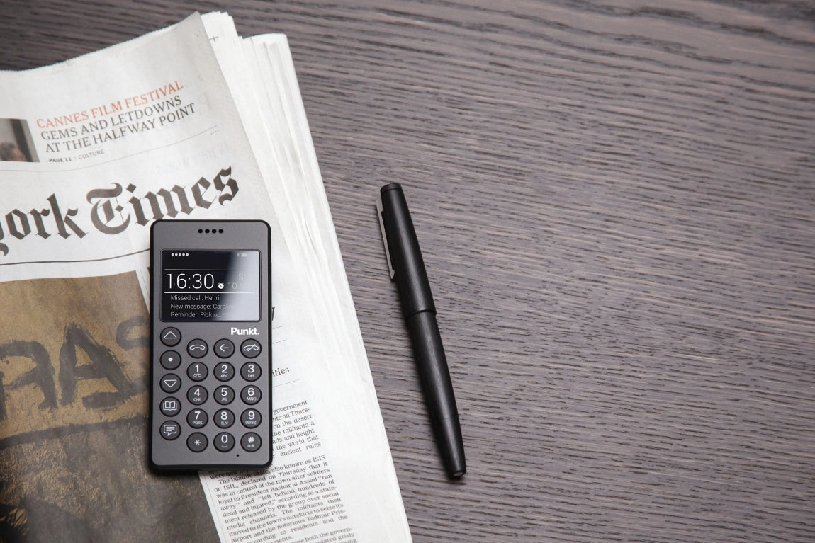 Minimalist mobile phone Punkt MP01 black on a newspaper background, with elegant design and clearly visible physical buttons.
