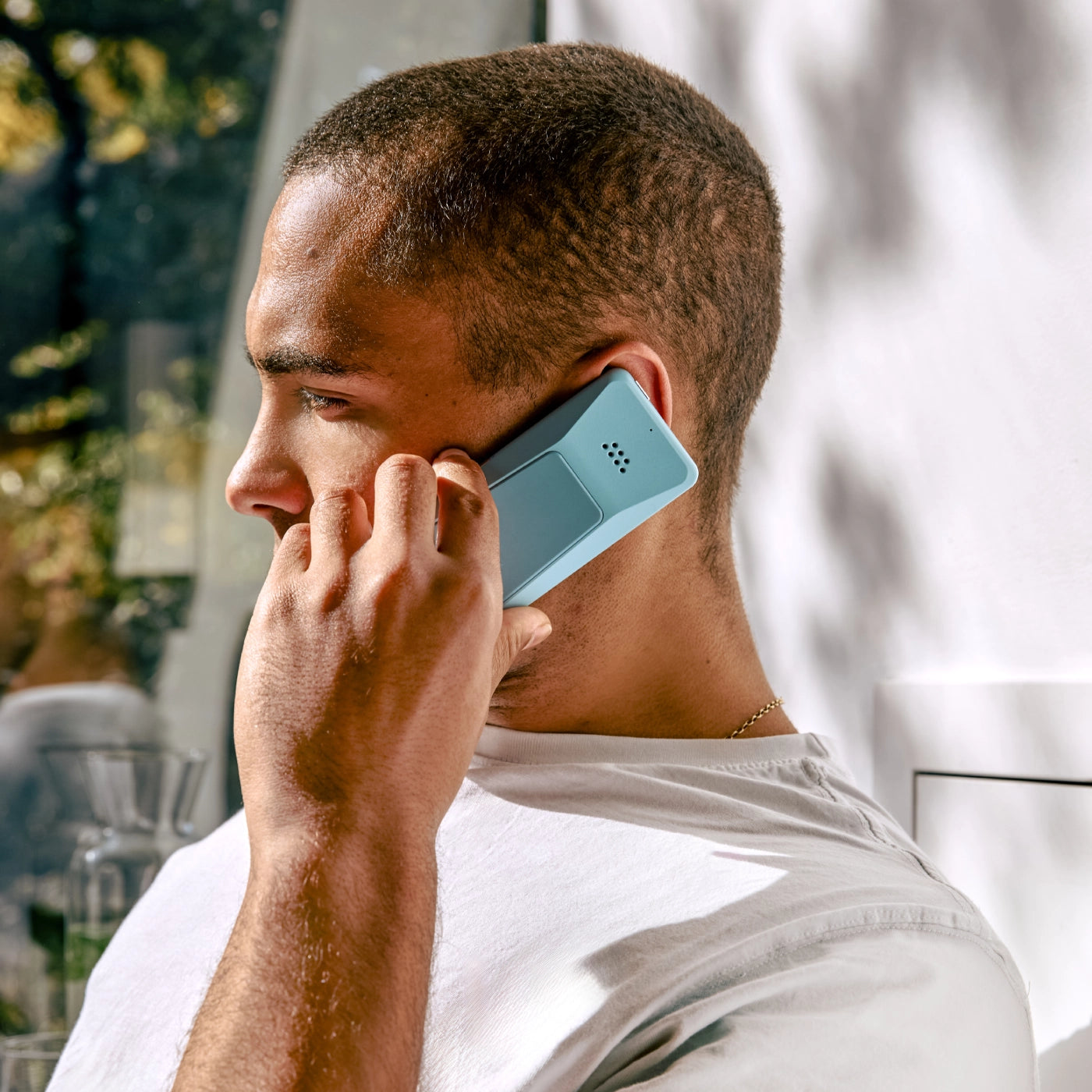 A man making a phone call using the blue Punkt. MP02, seated by a sunlit window.