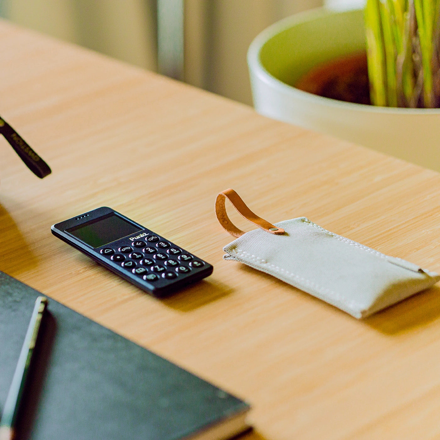 Punkt. MP02 phone and QWSTION case placed on a wooden desk next to a plant pot.