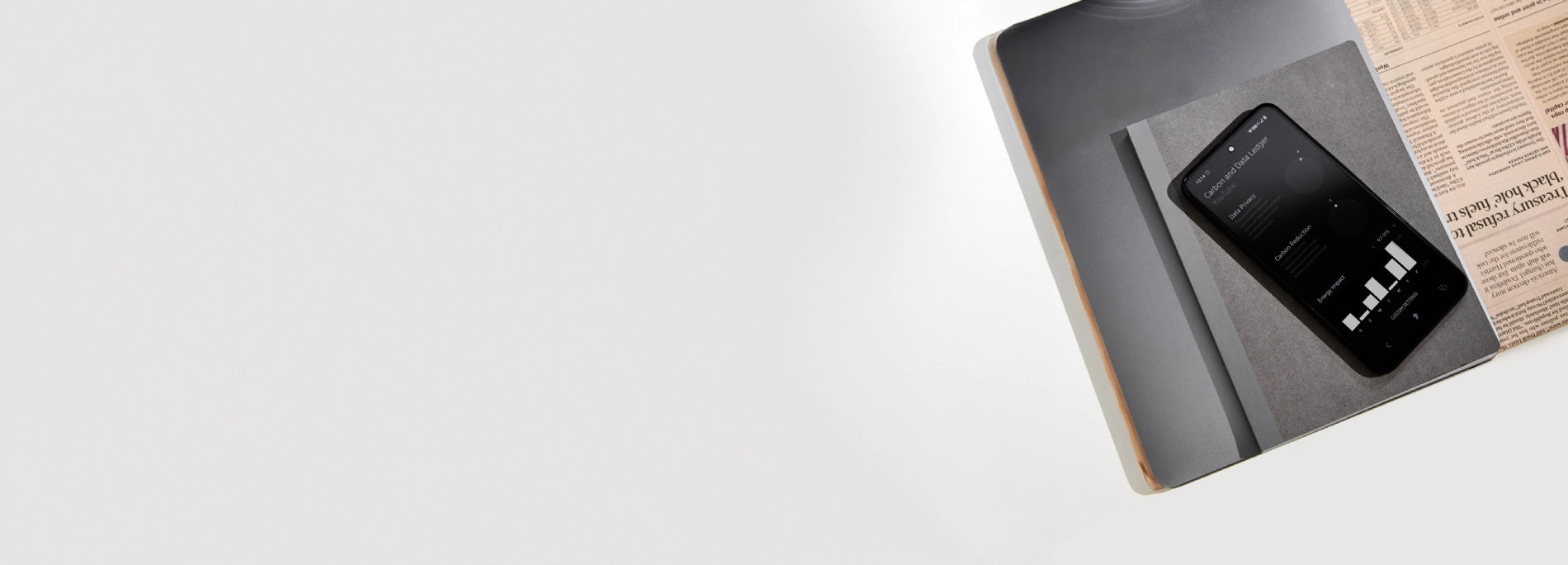 Vista dall’alto di un tavolo bianco con laptop, quaderno grigio e telefono che mostra grafici.