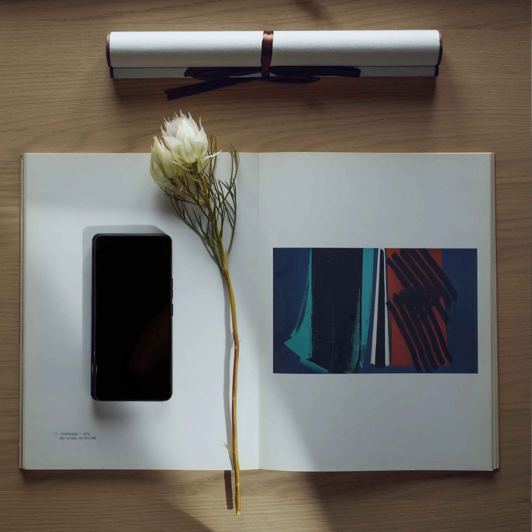 Open book with a smartphone, flower, and abstract art on a wooden surface