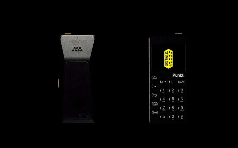 Two black Punkt. MP02 phones are shown against a black background: the back of the phone on the left features subtle Moncler branding, while the front-facing phone on the right displays the yellow Moncler Genius logo on its screen, emphasizing the sleek, minimalist design.