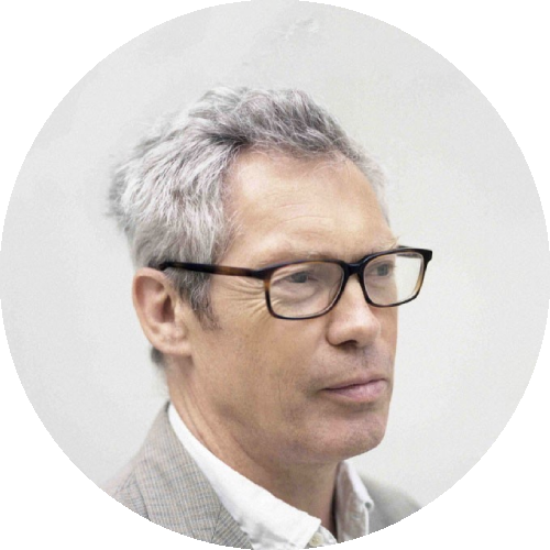 Circular portrait of a man with gray hair and glasses wearing a light suit and white shirt on a pale background.
