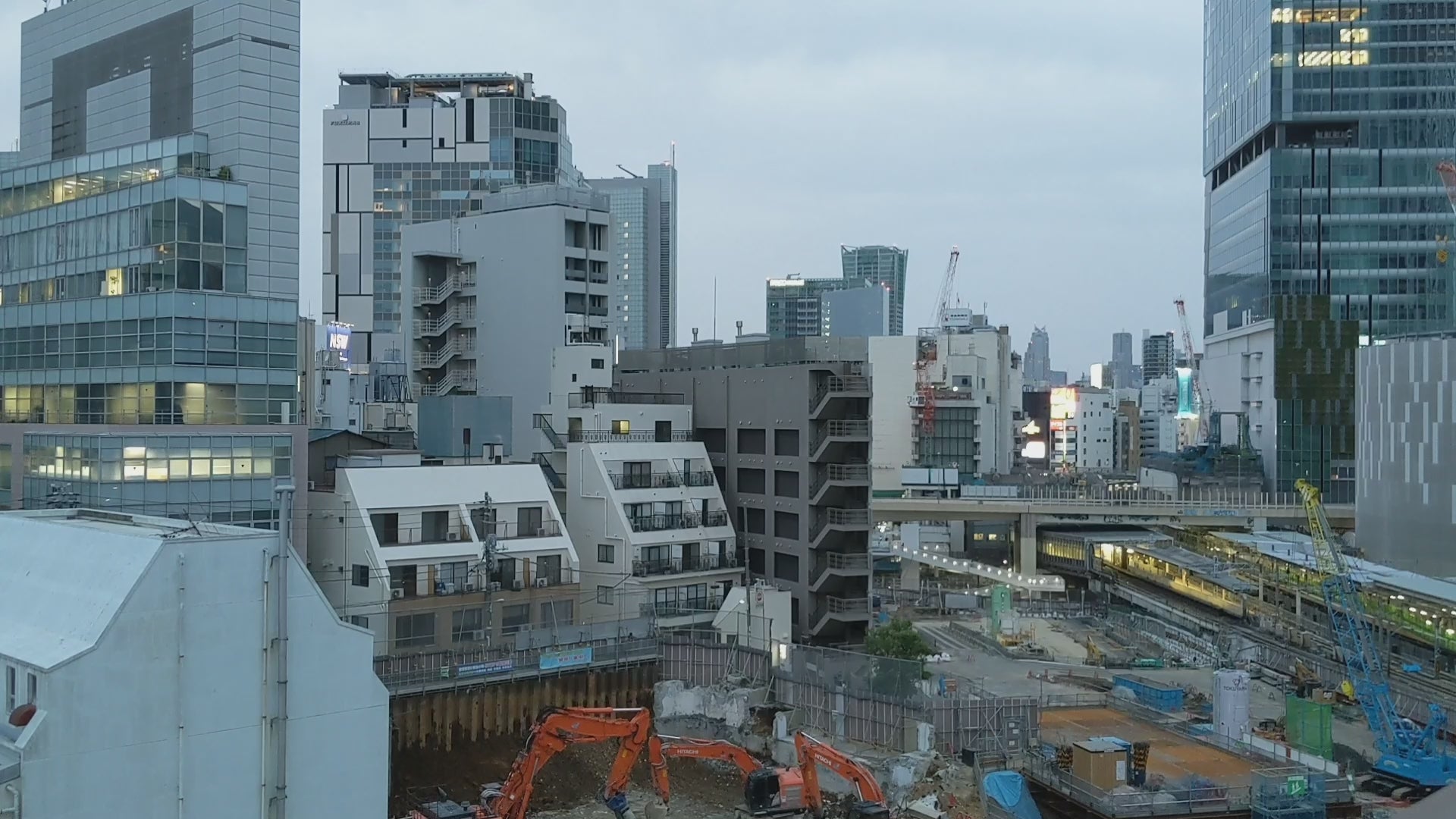 Video thumbnail showing a peaceful cityscape with modern high-rise buildings, cranes, and a train station under a cloudy sky, capturing an urban scene in soft daylight.