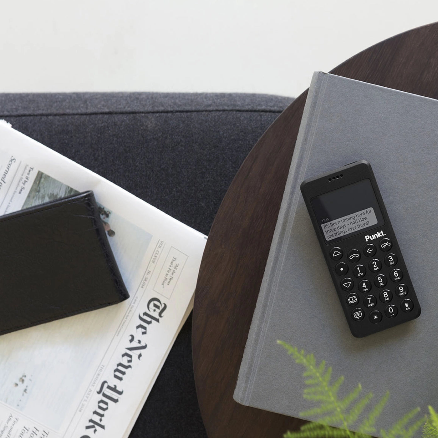 A compact black phone with round buttons and small screen displaying the time, placed on a light wooden table.