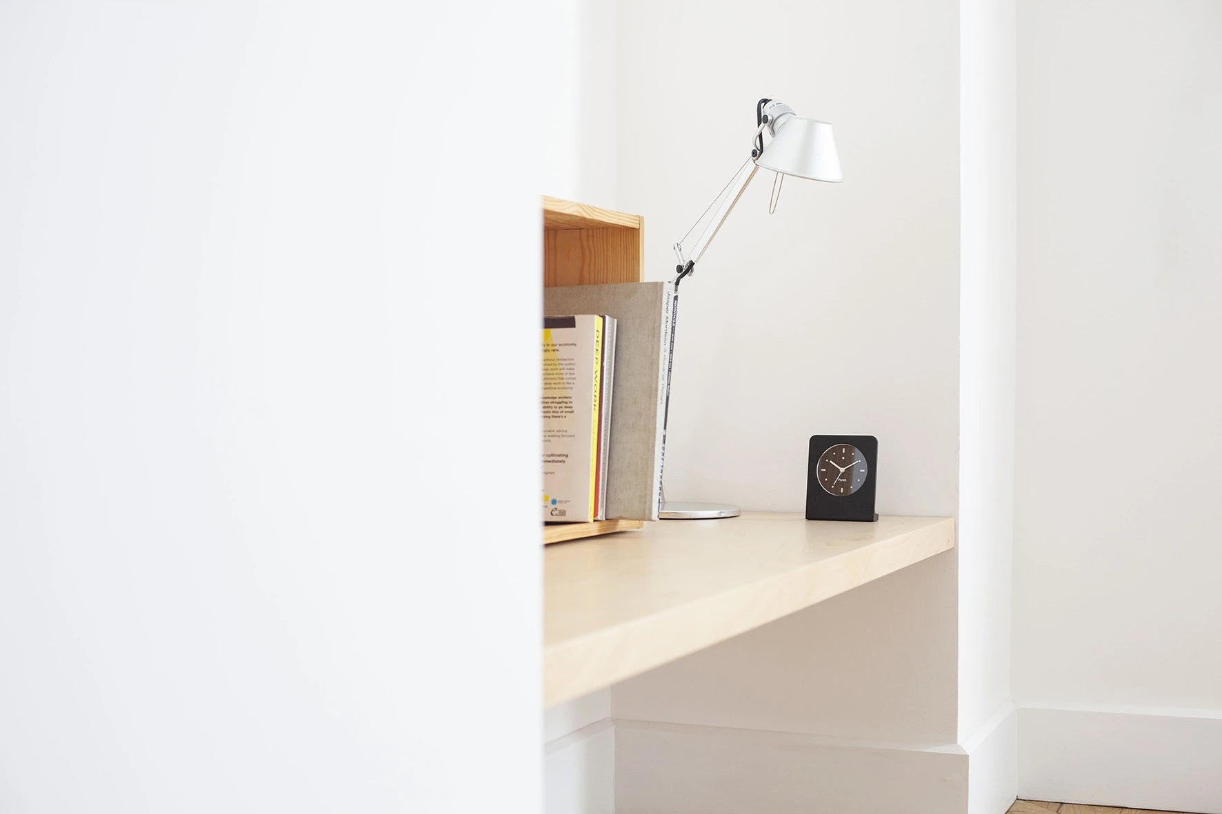Punkt AC02 alarm clock with pale blue second hand on a minimal desk next to a chrome reading lamp and vertical file rack.
