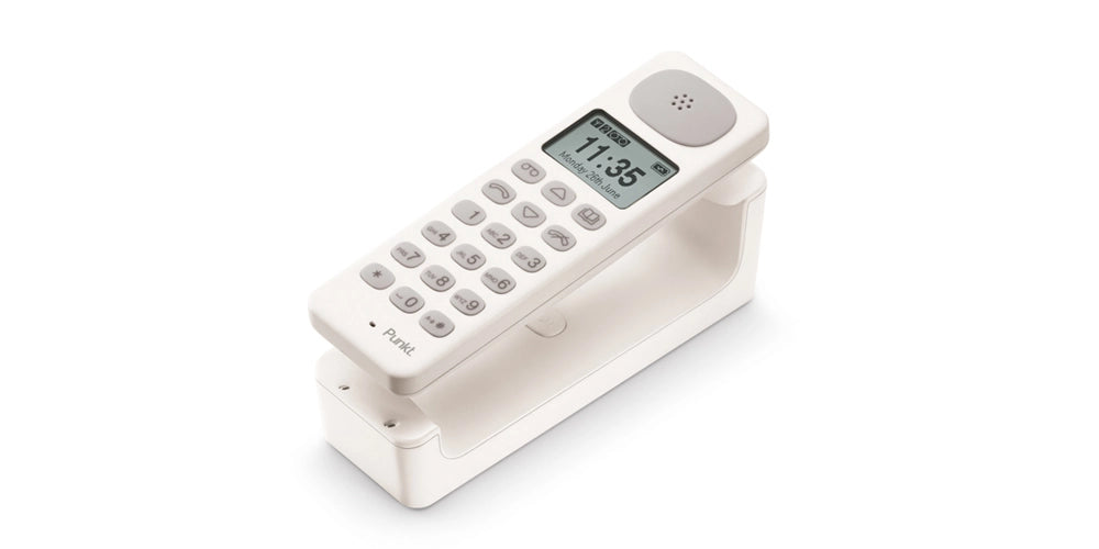 White Punkt. DP01 cordless phone resting in its minimalist charging base, with display showing time and date.