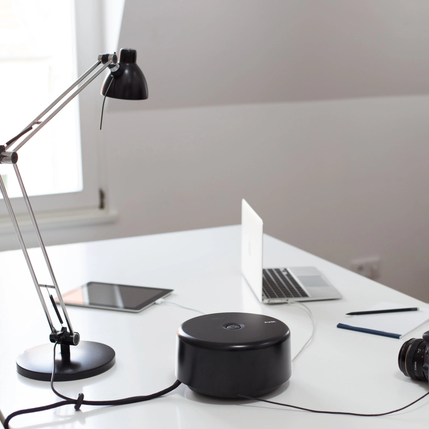 Side view of the Punkt. ES01 black power strip on a tidy desk, powering a laptop, tablet, and camera in a modern home office.