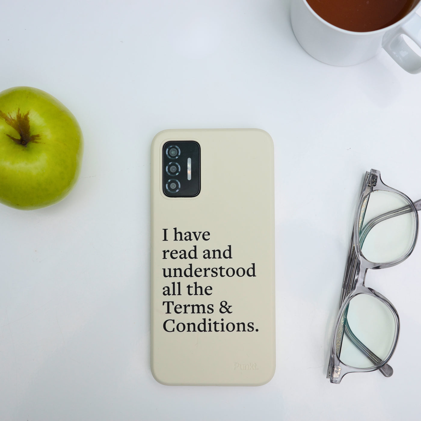 Punkt. MC02 in cream case with printed text, placed on a white surface near an apple, glasses, and a coffee mug.