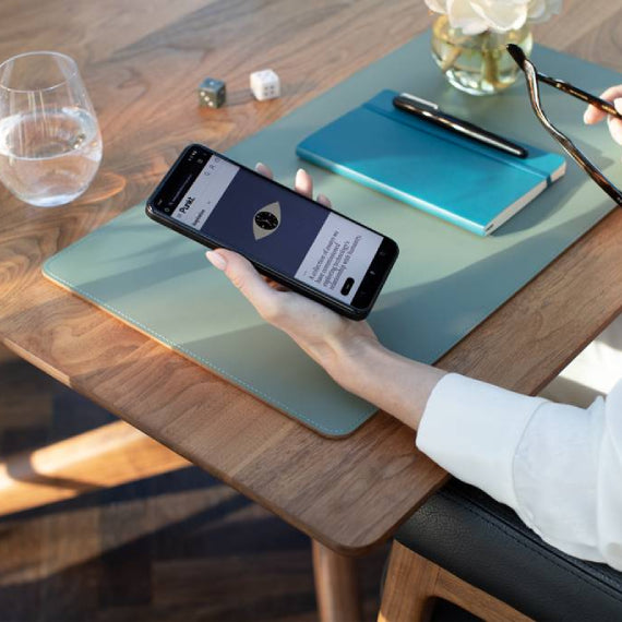 Person at a desk holding a smartphone with a website or app open, notebook and glass nearby.