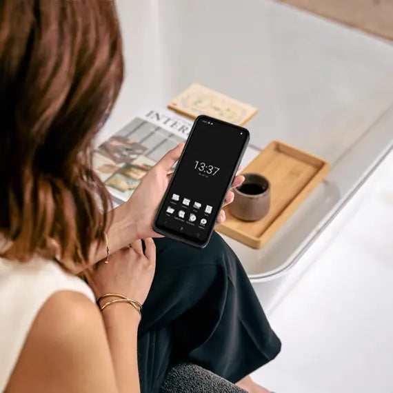 Person holding smartphone – Woman seated, holding a black Punkt. smartphone displaying a monochrome interface.