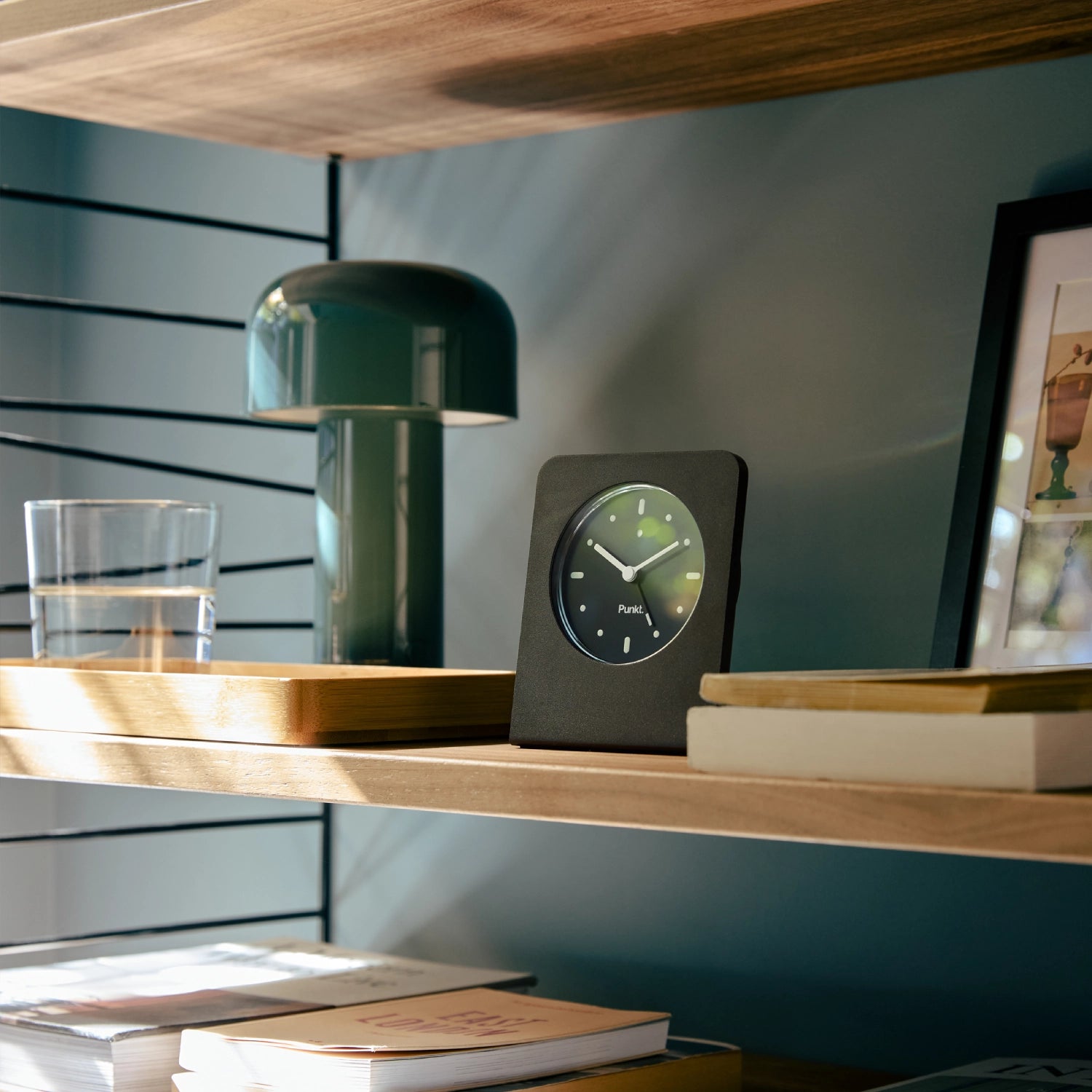 Punkt. AC02 minimalist alarm clock displayed on a wooden shelf in a modern home interior.