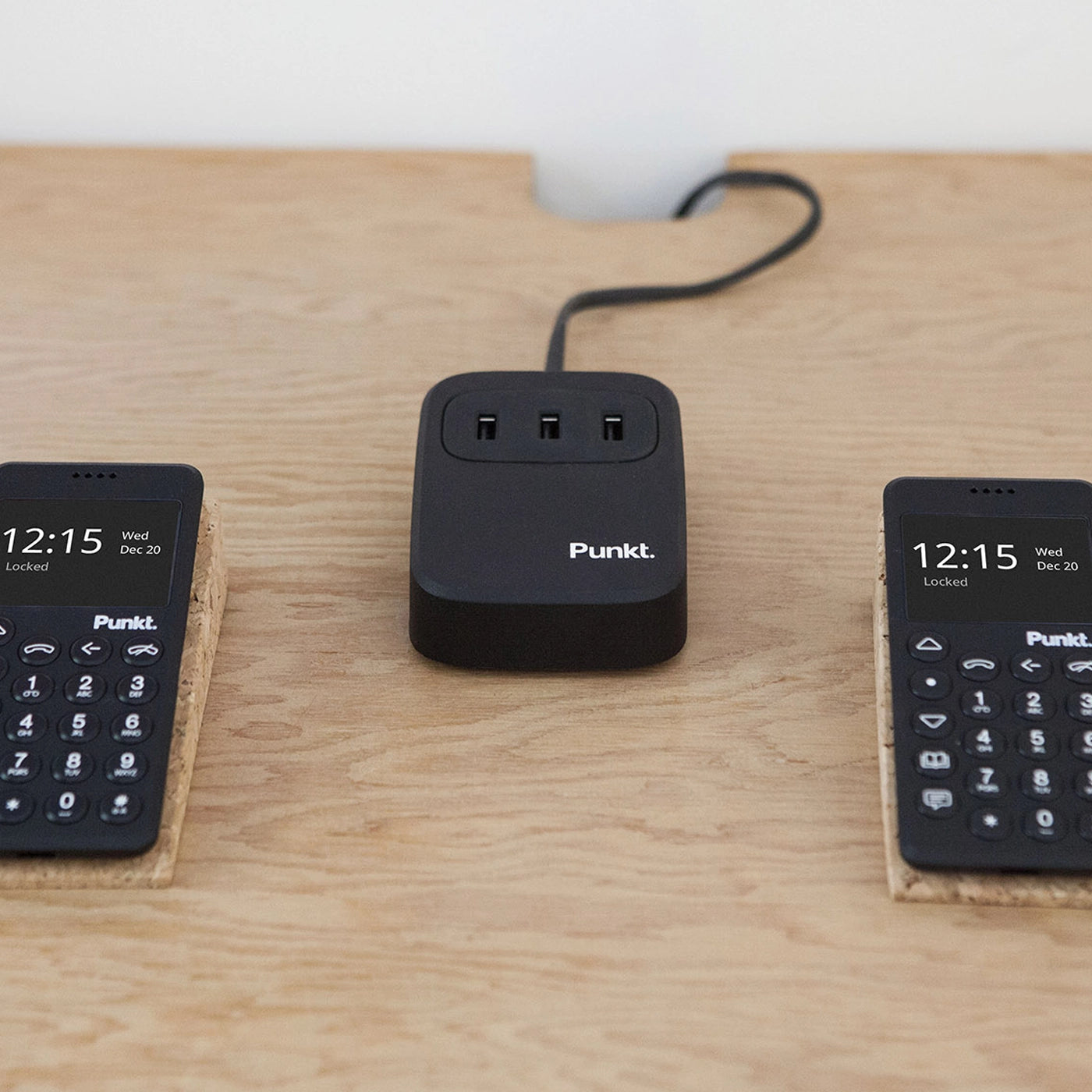 Punkt. UC01 minimalist 3-port USB charger shown on a desk with two MP02 phones connected.