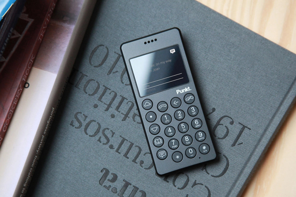 Punkt MP01 black phone resting on an open book, showcasing its minimalist design and tactile keypad.