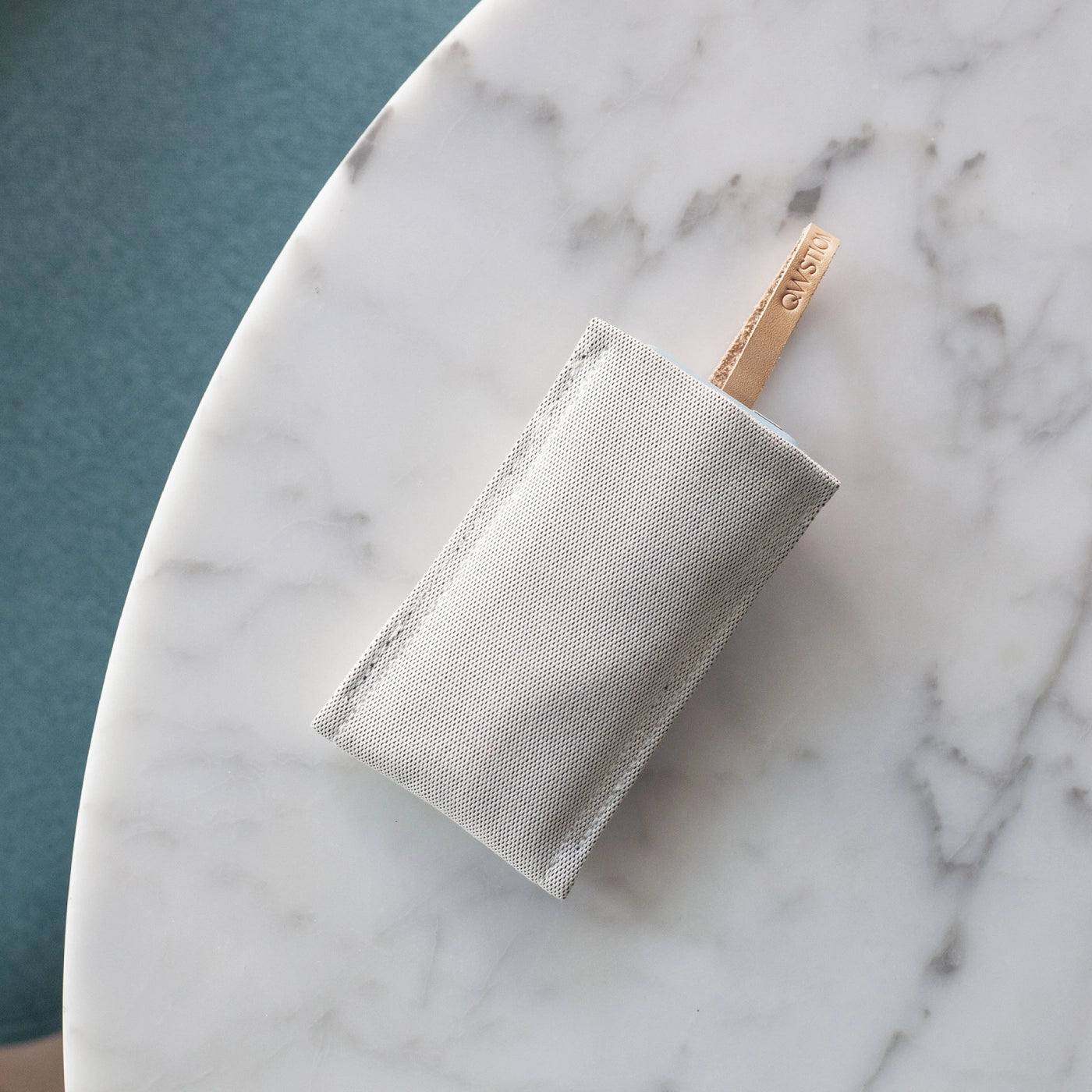 QWSTION grey protective case for Punkt. MP02 with leather loop, placed on a marble table.