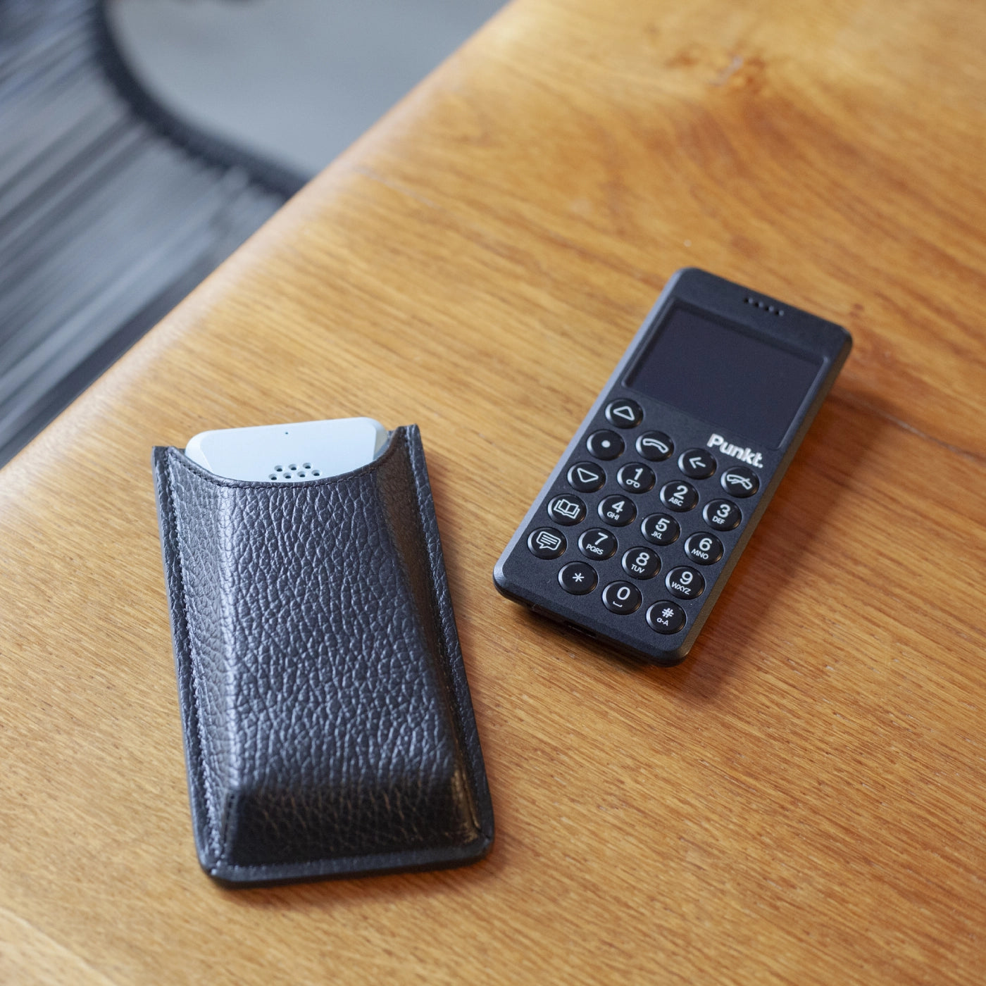 Punkt. MP02 phone next to its Danny P leather case on a wooden surface.