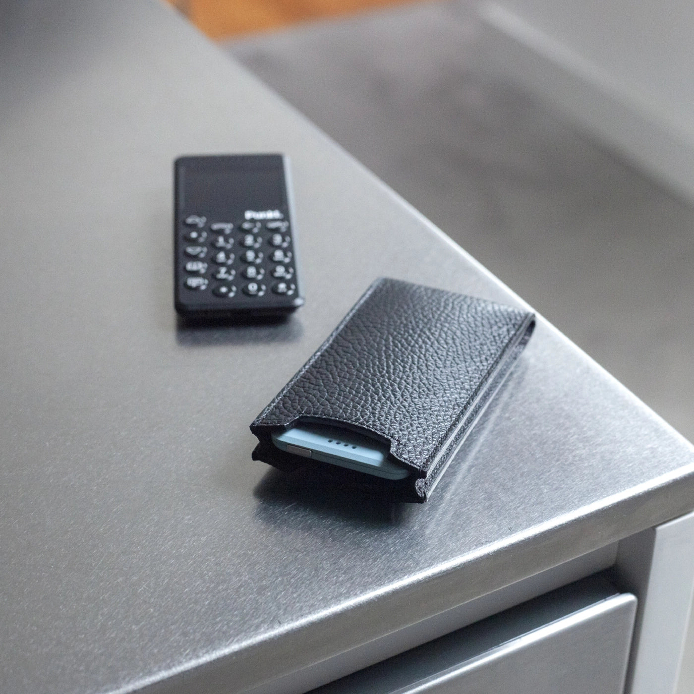 Danny P leather case for Punkt. MP02 placed on a metallic surface with the phone nearby.