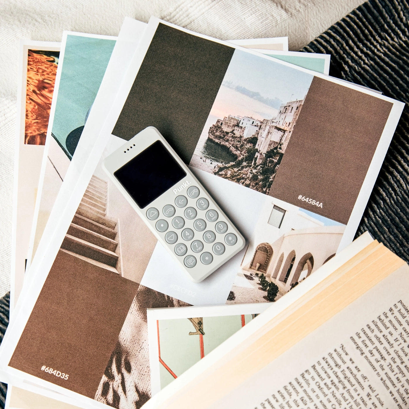 A white Punkt. MP02 mobile phone placed on printed design moodboards, showcasing architecture and color swatches.