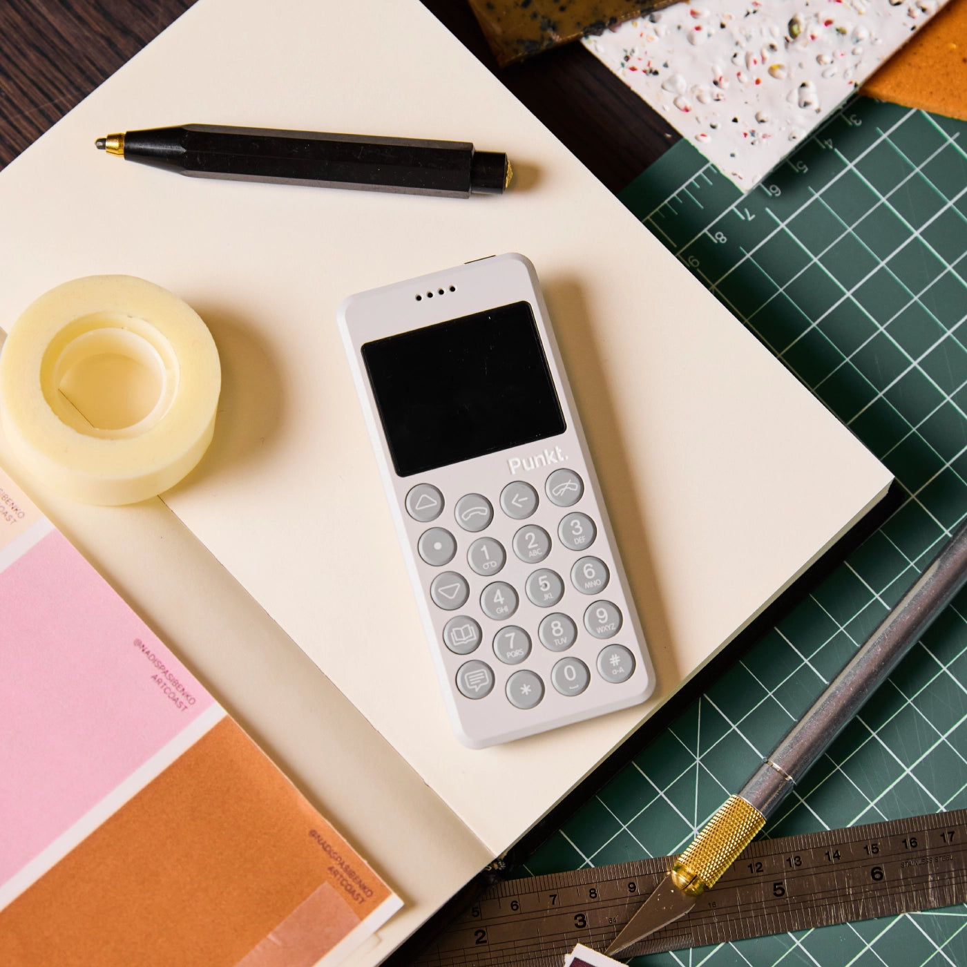 A black Punkt. MP02 phone placed neatly on a green cutting mat on a wooden desk.