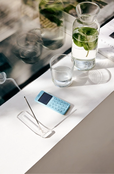 A blue Punkt. MP02 phone placed on a white windowsill beside a glass carafe and incense holder.