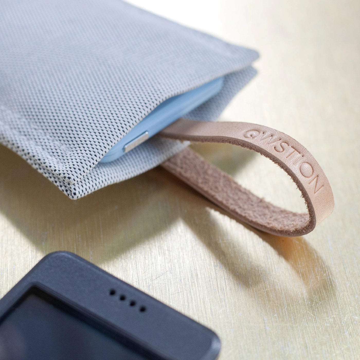 Close-up of the QWSTION case with a leather strap, partially revealing a light blue Punkt. MP02 phone inside.