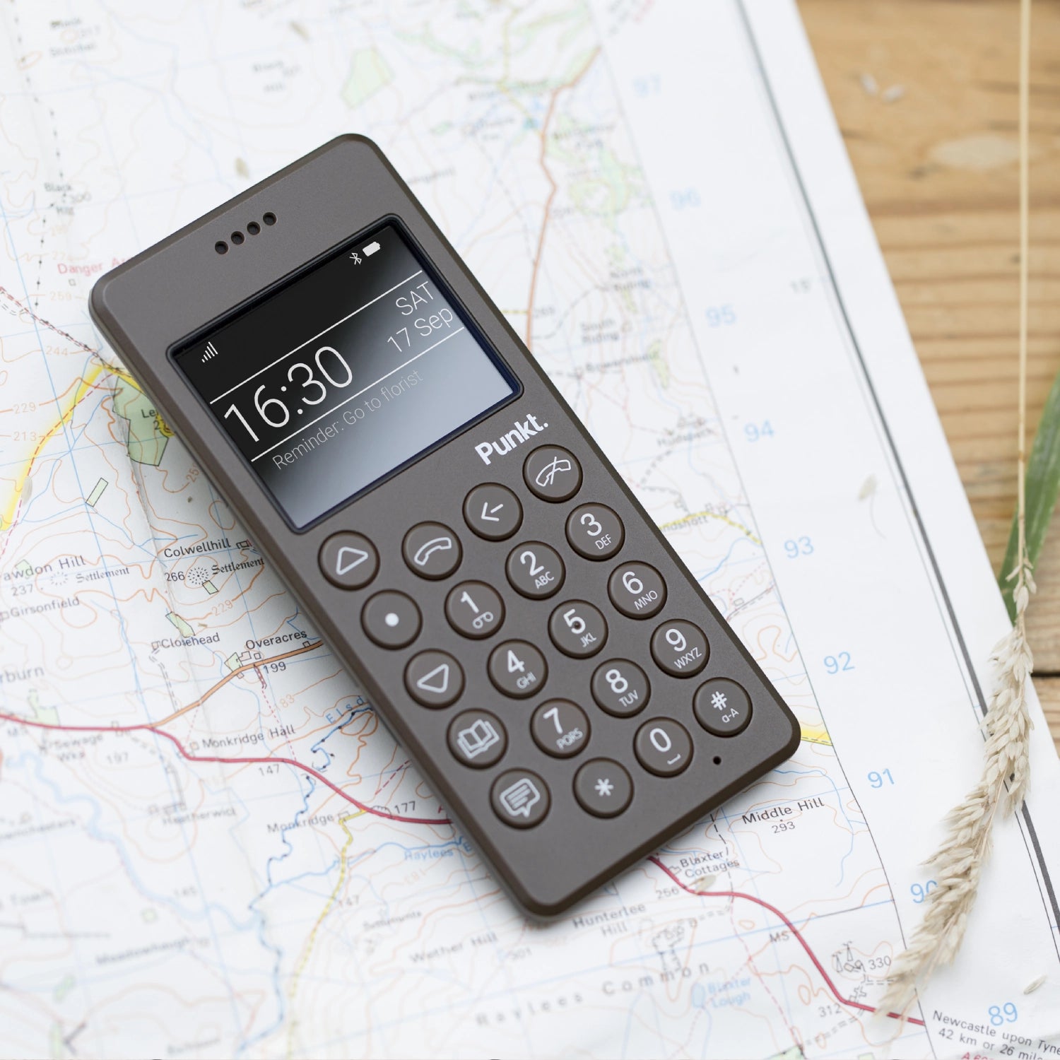 Punkt. MP01 mobile phone in brown, resting on a detailed map, showcasing its minimalist design and digital screen.