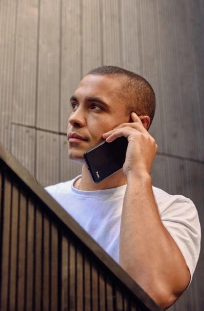 Young man in a white t-shirt talking on a Punkt. mobile phone while standing against a modern wooden wall.