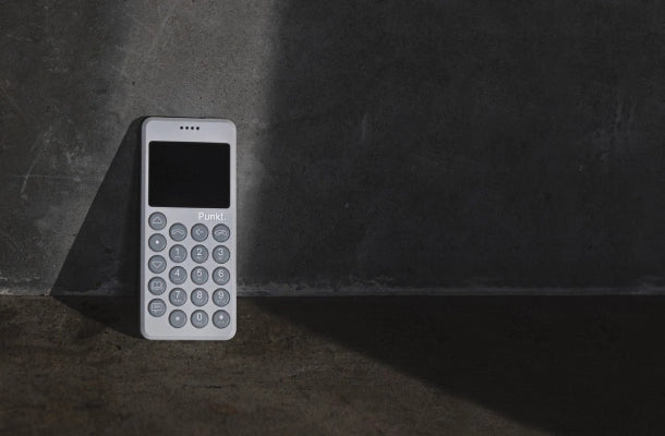 Light grey Punkt. MP02 phone standing upright against a concrete wall, partially lit by a dramatic beam of light.