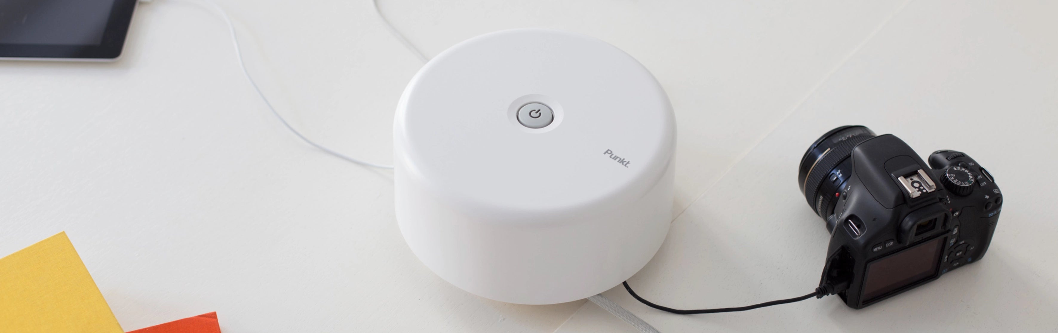 Punkt. ES01 white power extension socket on a white surface, with connected cables powering a tablet and a DSLR camera.