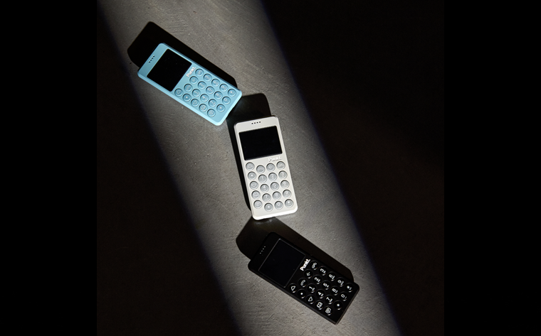 Three Punkt MP02 dumb phones in black, white, and blue colors, arranged diagonally under a beam of light on a dark surface.