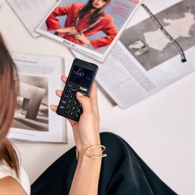 Woman holding a black Punkt MP02 phone, surrounded by open magazines, emphasizing privacy and minimalism